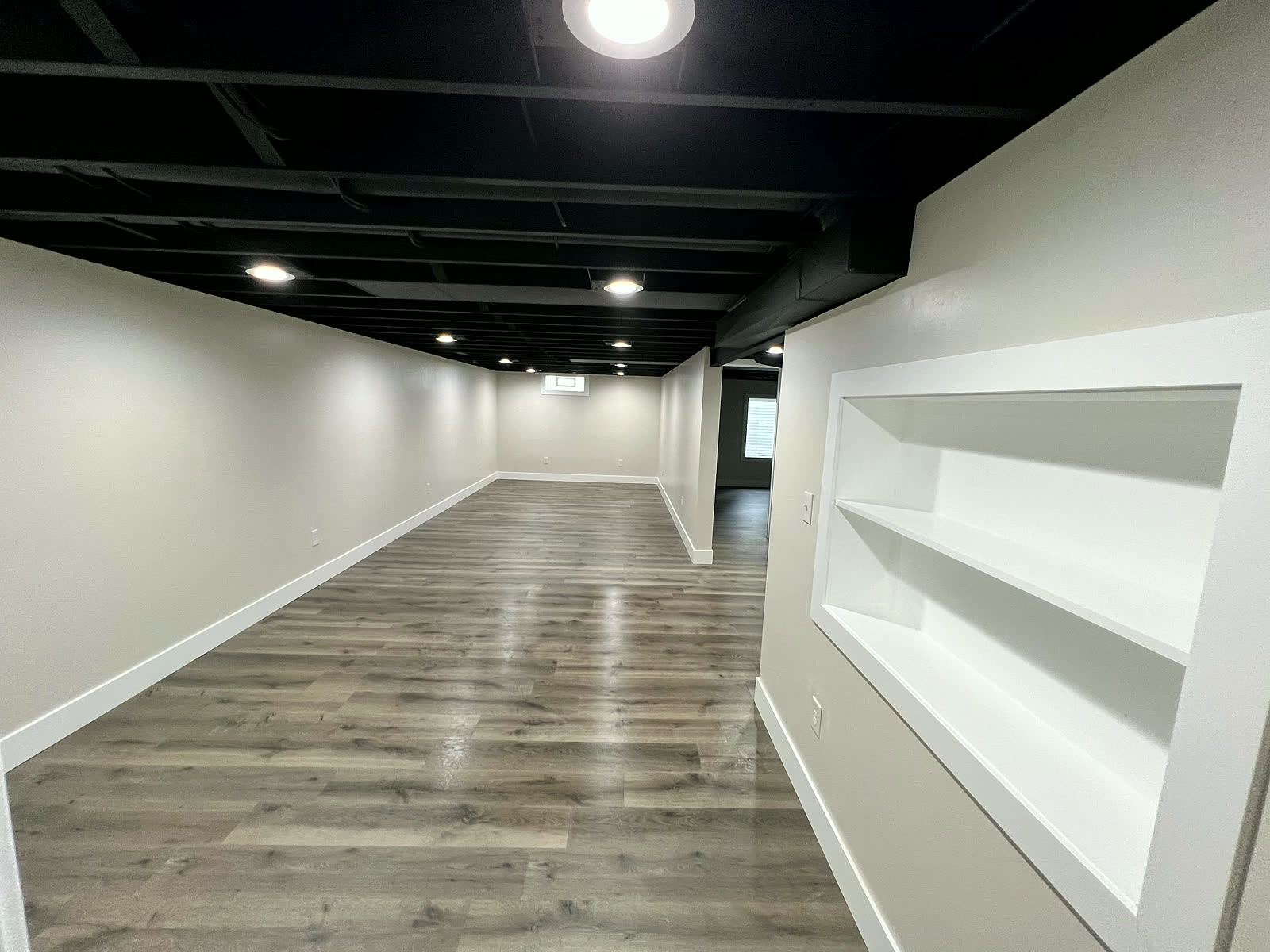Finished basement hallway with built-in shelving niche and LVP flooring