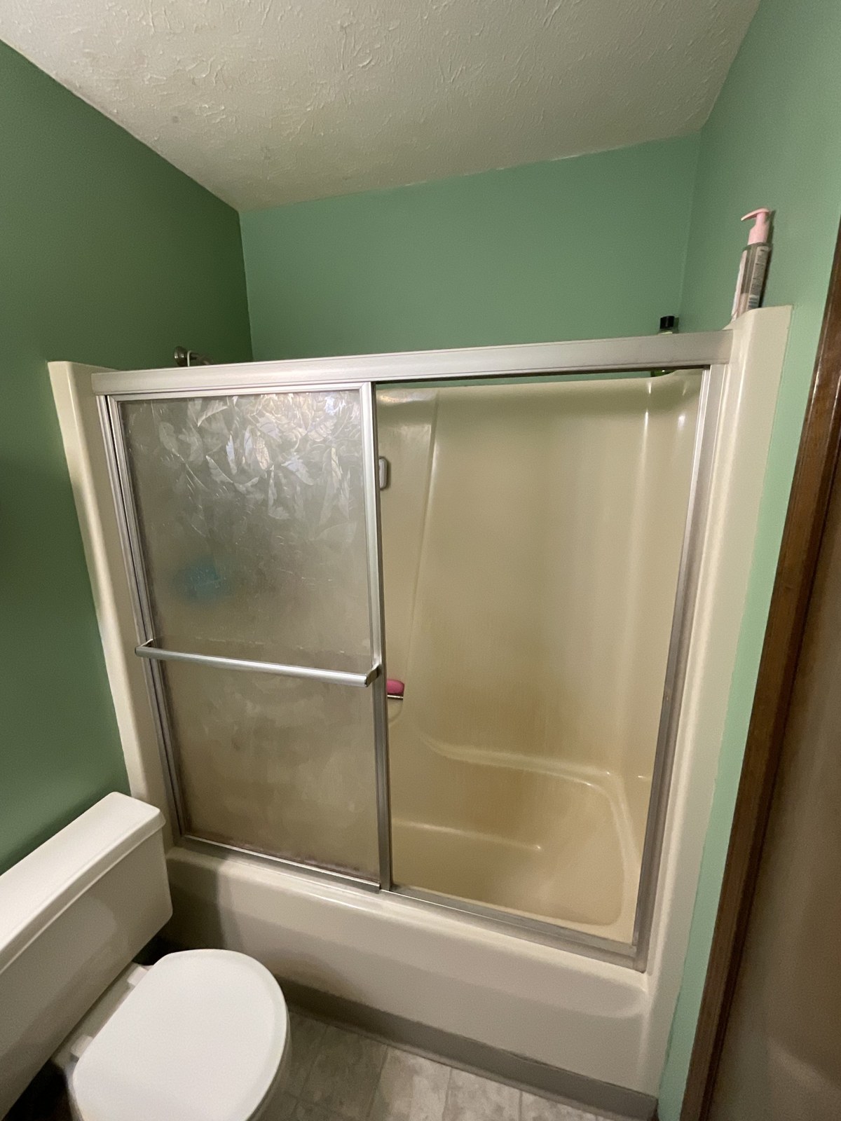 Bathroom before remodel — dated sliding glass tub doors