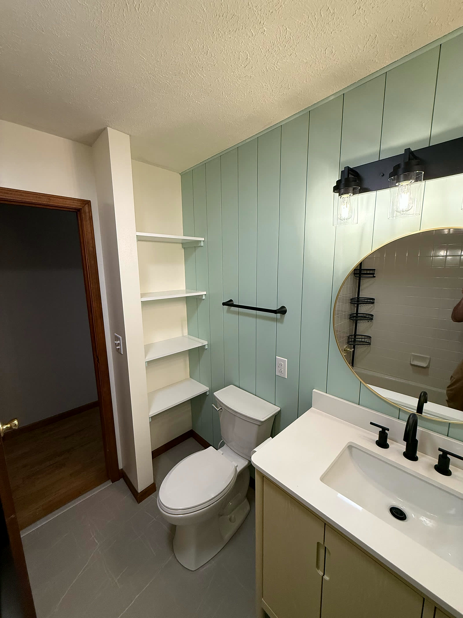 Bathroom with sage shiplap accent wall, round mirror and floating vanity