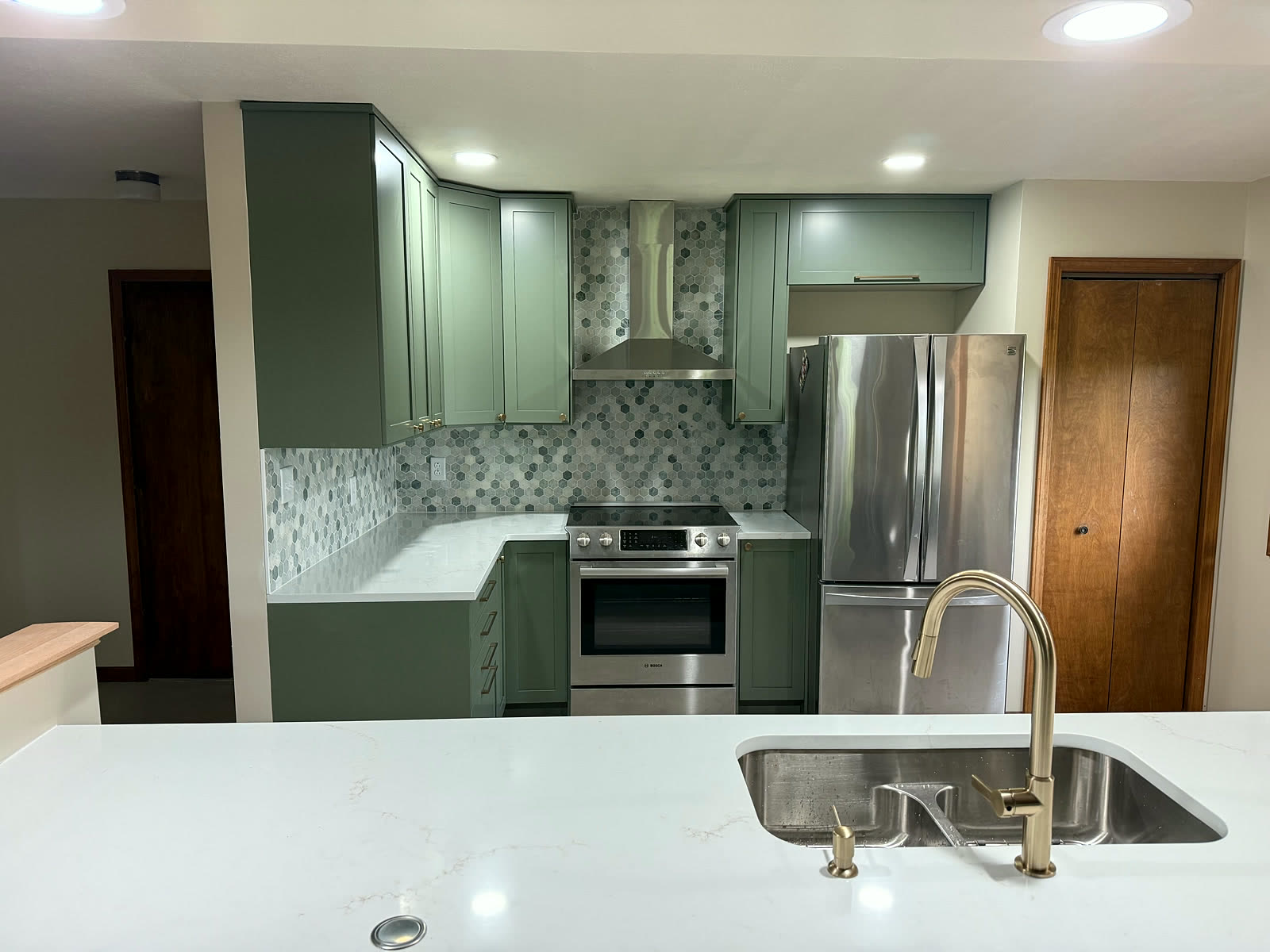 Sage-green kitchen with double-bowl island sink and mosaic backsplash