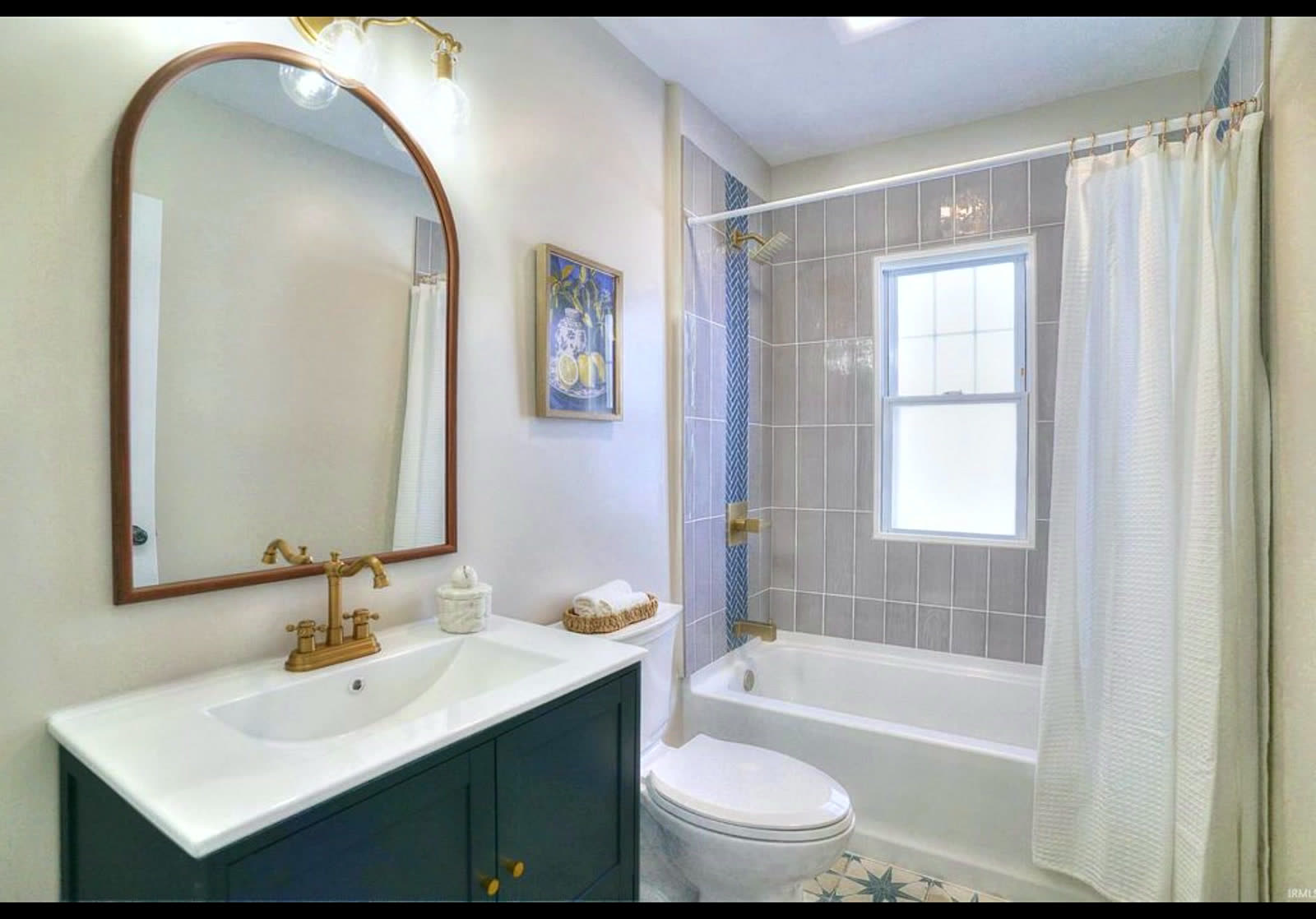 Bathroom with blue vanity, gold faucet and arched mirror